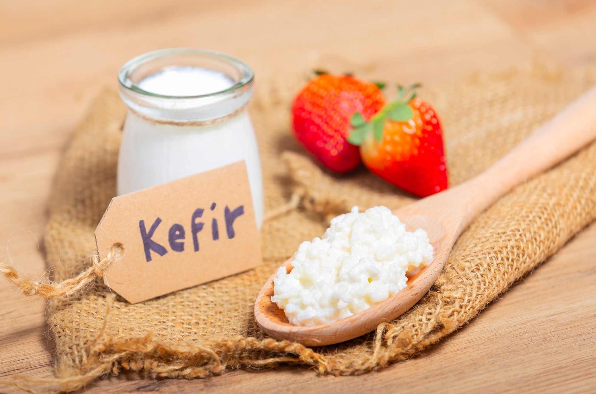 Grains de k&eacute;fir dans une cuill&egrave;re en bois devant des tasses de parfaits au yaourt au k&eacute;fir.