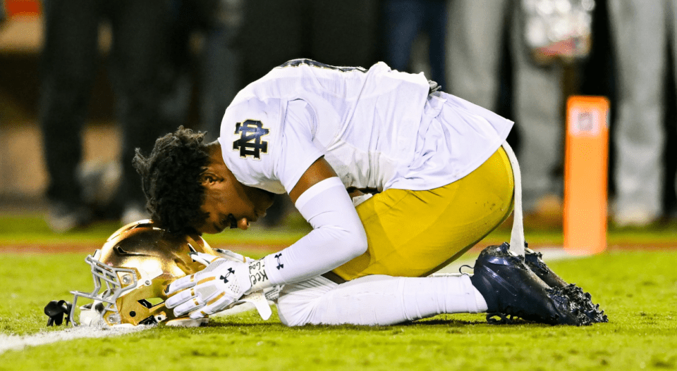 Un joueur de football de Notre-Dame s'agenouille sur le terrain dans un moment de d&eacute;sespoir, posant sa t&ecirc;te sur son casque, exprimant sa d&eacute;ception apr&egrave;s un match.