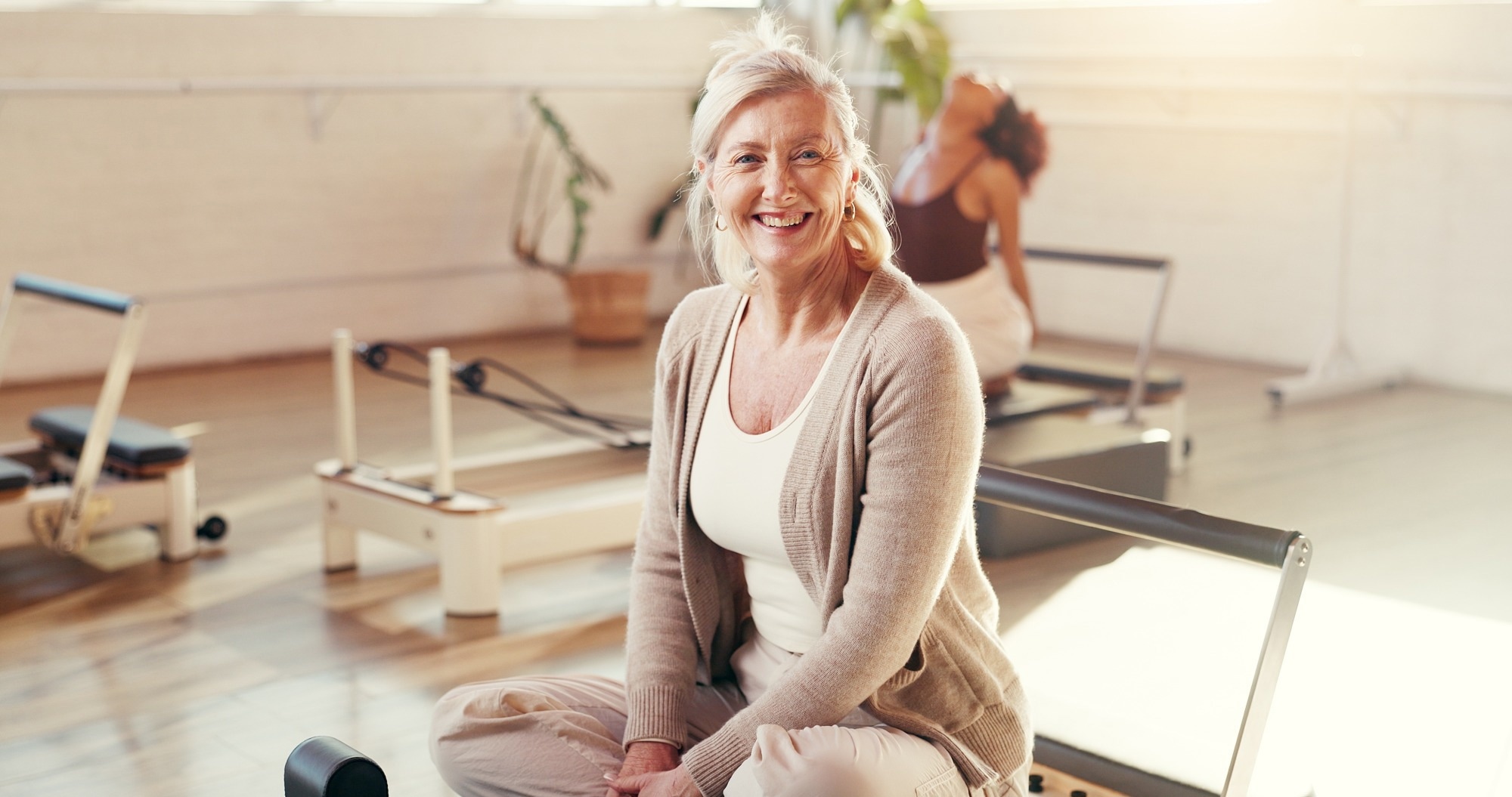 femme plus &acirc;g&eacute;e assise sur un &eacute;quipement Pilates. souriant
