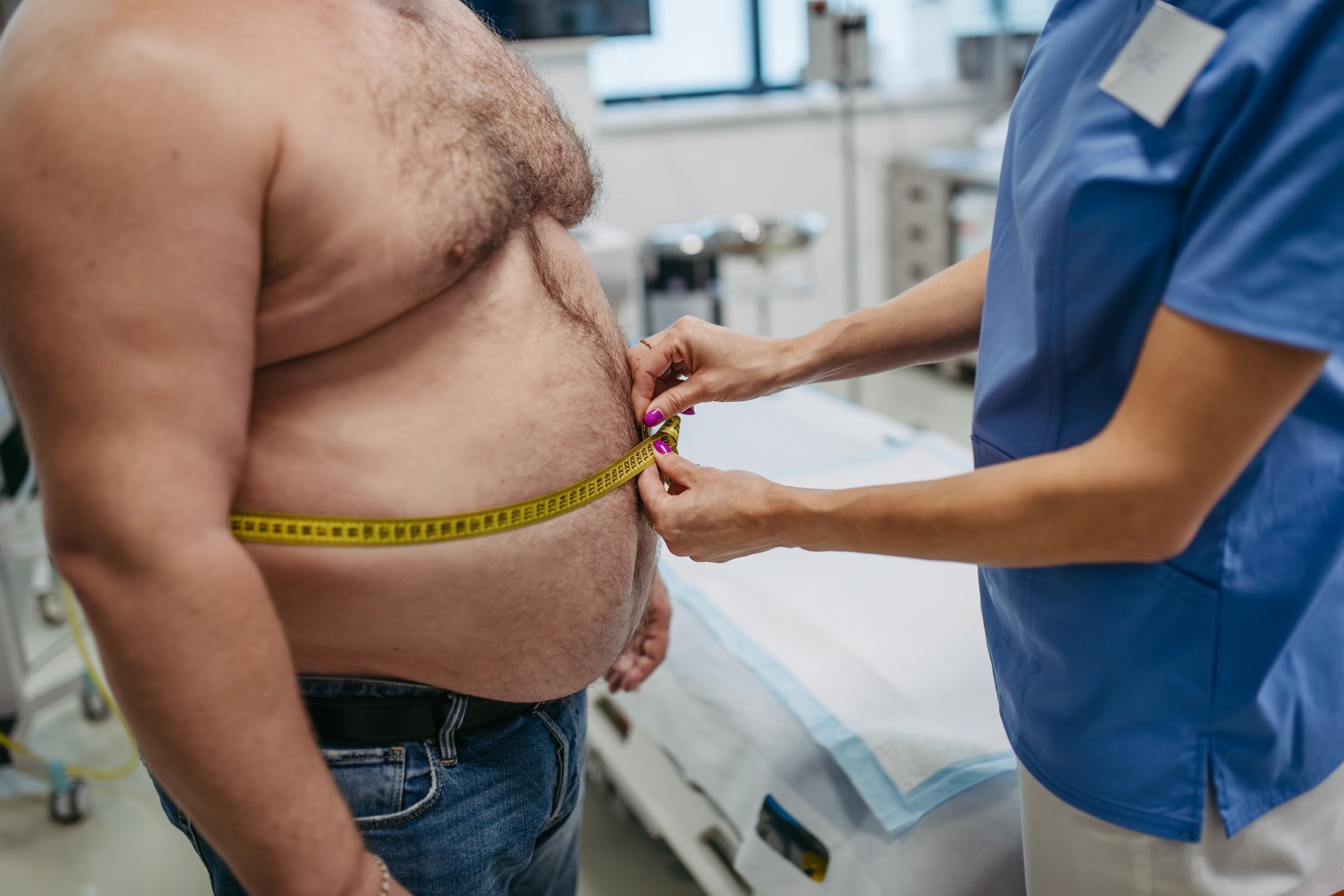 Femme m&eacute;decin mesurant la taille d'un patient en surpoids &agrave; l'aide d'un ruban &agrave; mesurer. L'ob&eacute;sit&eacute; touche les hommes d'&acirc;ge moyen