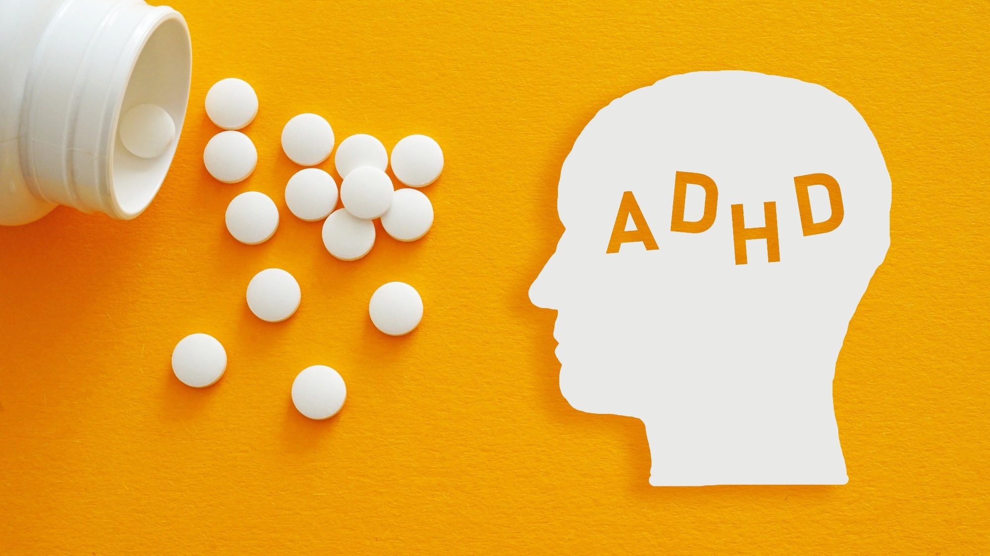Silhouette blanche de la t&ecirc;te du TDAH &agrave; c&ocirc;t&eacute; de comprim&eacute;s de m&eacute;dicaments dispers&eacute;s sur fond jaune, illustrant le traitement stimulant du trouble d'hyperactivit&eacute; avec d&eacute;ficit de l'attention.